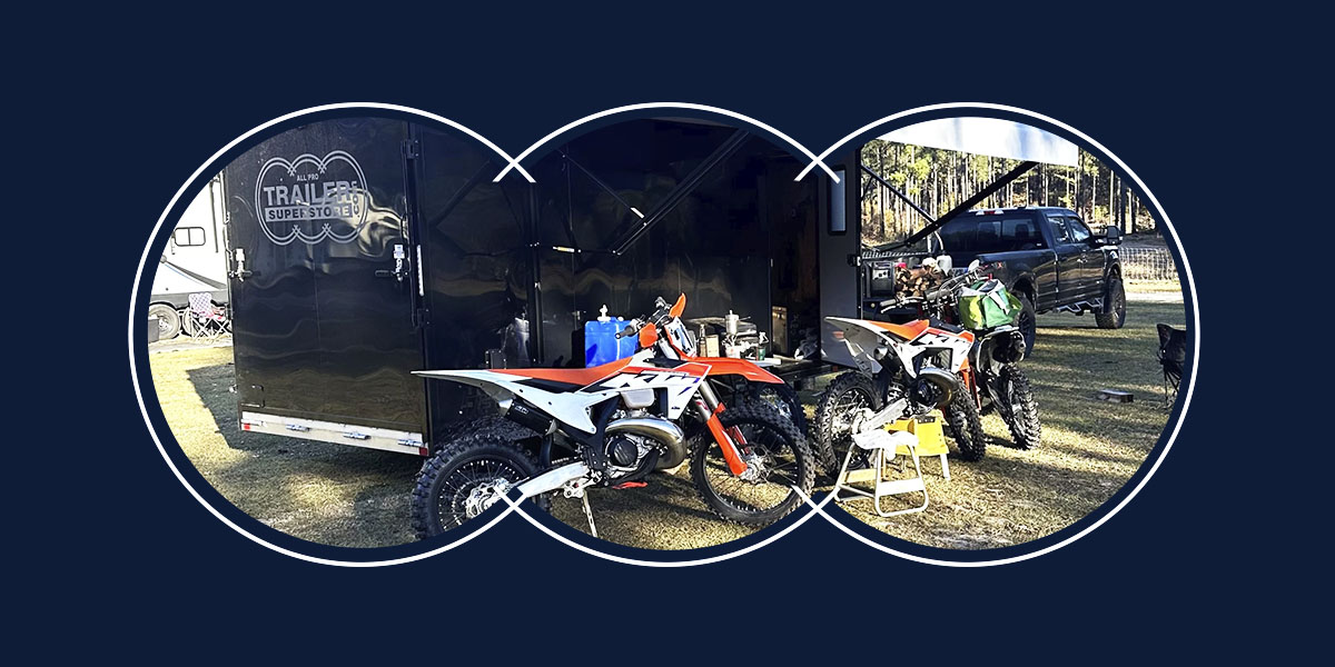 A black motorcycle trailer with three dirt bikes next to it