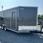 a black and silver trailer is parked in a gravel lot