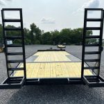 a trailer with a wooden deck and stairs is parked in a gravel lot