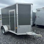 a black and silver trailer is parked in a gravel lot