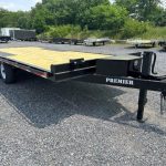 a trailer with a wooden deck is parked in a gravel lot .