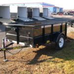 a black trailer is parked in the grass in front of a building .