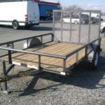 a small trailer is parked in a gravel lot next to a white van