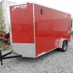 a red homesteader trailer is parked in a gravel lot .