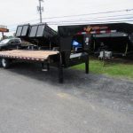 a flatbed trailer is parked on the side of the road next to a dump trailer .