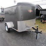 a black trailer is parked on the side of the road next to a dump trailers .