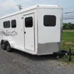 a white horse trailer is parked in a gravel lot .