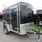 a black trailer is parked on the side of the gravel parking lot