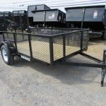 a trailer is parked in a gravel lot next to dumpsters .