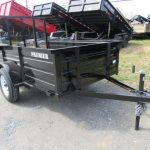 a black trailer is parked in a grassy field next to a dump truck .