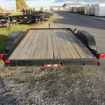 a trailer with a wooden deck is parked in a gravel lot