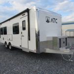 a white trailer is parked in a gravel lot in front of a building .