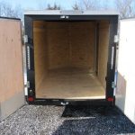 an empty trailer with the doors open is parked in a gravel lot .