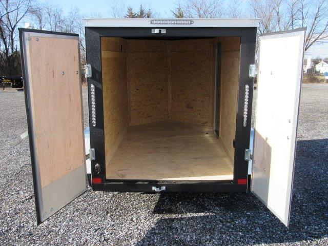 an empty trailer with the doors open is parked in a gravel lot .