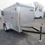 a silver trailer is parked in a gravel lot