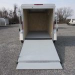 the back of a trailer with the ramp open in a gravel lot .