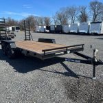 a trailer with a wooden deck is parked in a gravel lot .