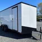 a white and black trailer is parked in a gravel lot