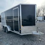 a black and silver trailer is parked in a gravel lot