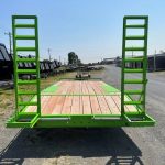 a green trailer with a wooden deck is parked on the side of the road .