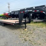 a black flatbed trailer is parked in a gravel lot .