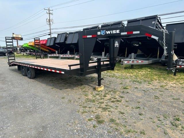 a black flatbed trailer is parked in a gravel lot .