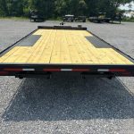 a trailer with a wooden deck is parked in a gravel lot .