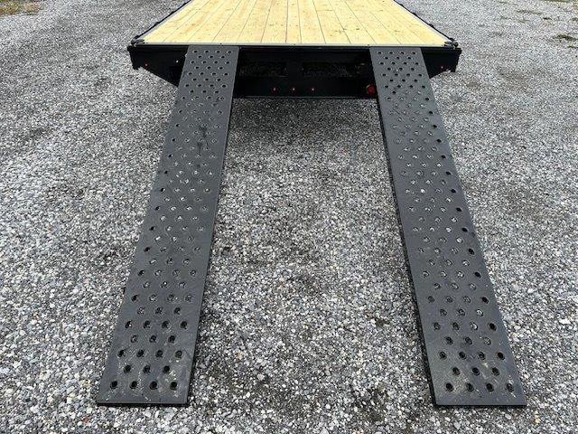 a trailer with ramps attached to it is sitting on top of a gravel road .