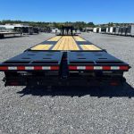 a trailer with a wooden deck is parked in a gravel lot