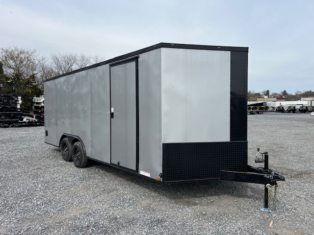 a gray and black trailer is parked in a gravel lot