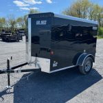 a black car-mate trailer is parked in a gravel lot